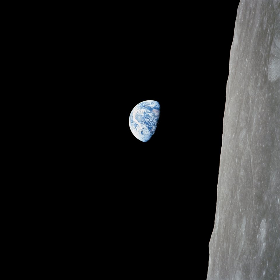 Earthrise in its original orientation: the half-lit blue Earth in black space, with the grey lunar surface running vertically along the right edge.