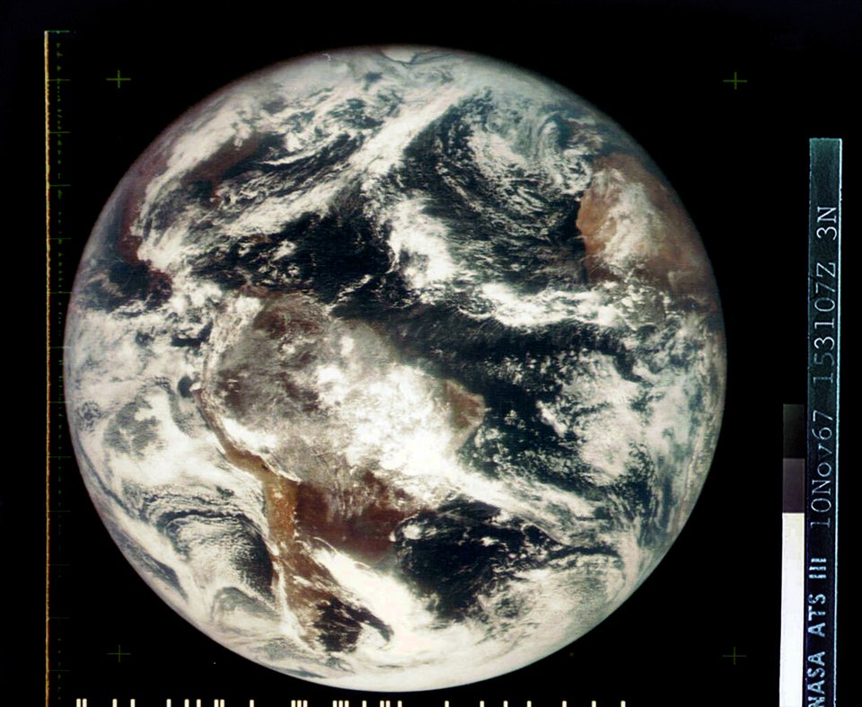 A grainy colour image of the whole Earth, the Americas faintly visible under swirls of white cloud against black space