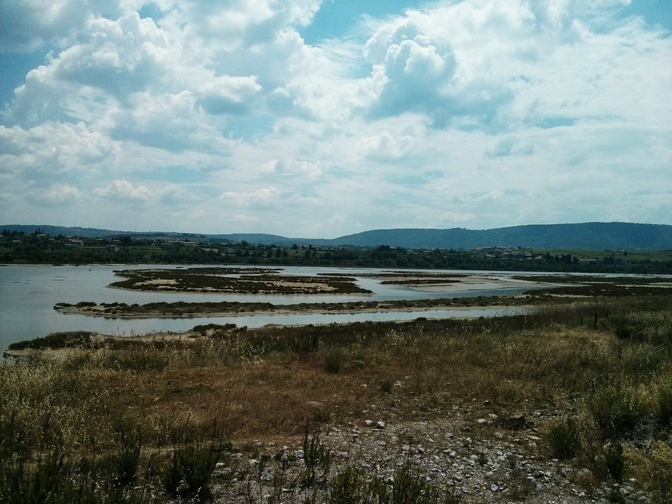 A shallow brackish lagoon with low islets and reeds under a cloudy sky, with hills on the horizon.